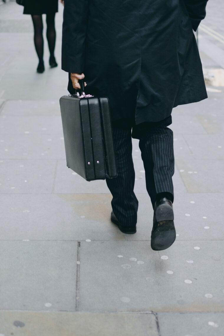 Person carrying suit case while walking on pavement